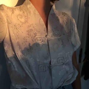 Vintage silkesskjorta - Vit silkestopp i östasiatisk design, kan inte riktigt placera.. Vintage, mycket bra skick utöver en knapp som är lite lös. Köparen står för frakt 60kr.