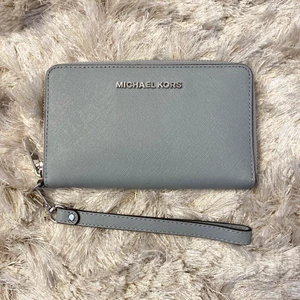 Äkta Michael Kors plånbok, HELT NY - Äkta Michael Kors plånbok i grå/ljus blå färg! Den kan även användas som en clutch då den har ett armband, perfekt för en utekväll! Den är helt oanvänd och har kvar carecard i. Värde 1660 i butik men jag säljer den för 450 kr! Köparen står för frakten 🥰