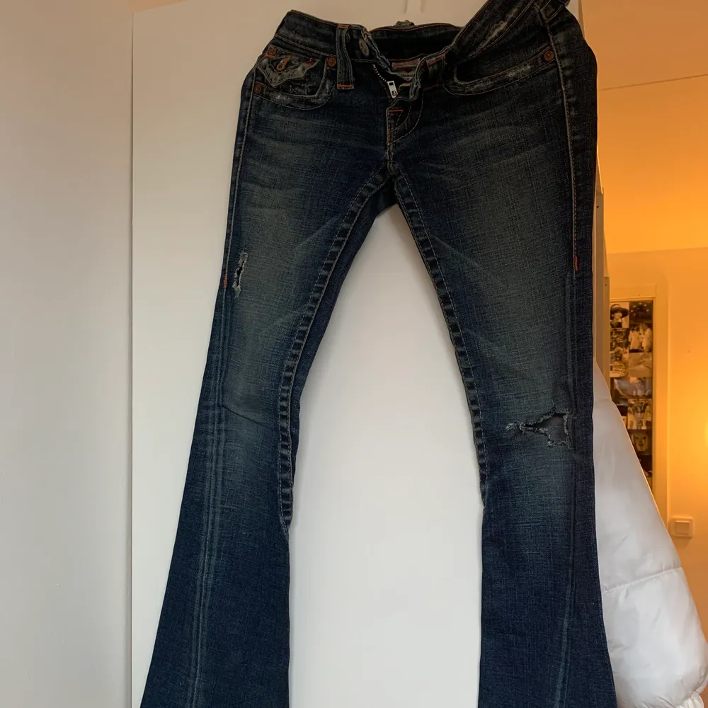 Lågmidjade mörkblåa jeans från märket true religion. Tyvärr alldeles för små och korta för mig som är 165, säljs pga det. Har två hål, slitningar i vardera ben.. Jeans & Byxor.