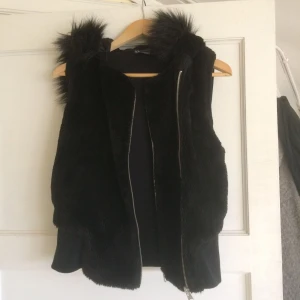  - Mysig väst i varmt mjukt tyg med stor mysig luva+fuskpäls. Fuskpälsen på luvan är avtagbar och västen passar XS-M beroende på hur man vill att den ska sitta. 