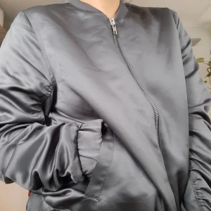 Grå bomberjacka strlk 38 - 🎗 grå tunn bomberjacka från WERA stockholm i strlk 38. Satin. Ihopdragning i ryggen och på armarna, ger snygg passform.75 kr exkl frakt