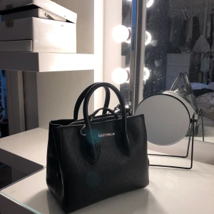 Coccinelle väska - Säljer min Coccinelle Farisa väska, nästan aldrig använd, därför jag säljer den. Syns kanske inte så tydligt på bilderna men väskan har även ett axelband. Väskan är i nyskick. Nypris: 3500kr.                 Vid snabb affär kan pris diskuteras 