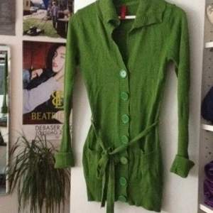 Mossgrön kofta med stora knappar och stickat bälte
