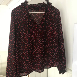 Prickig blus - En svart och röd prickig blus från Gina tricot, knappt använd, men pyttelitet hål vid halsknytningen annars bra tillstånd. Jätteskönt flowy material i storlek 36. Frakt tillkommer