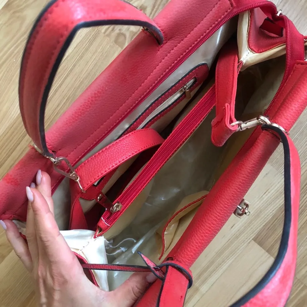 En röd handväska i (oäkta) läder med guldiga dragkedjor och smådetaljer. Axelrem medföljer. Aldrig använd. . Väskor.