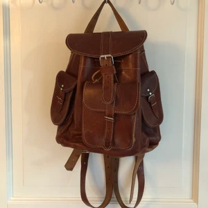 Vintage ryggsäck - Vintage ryggsäck i äkta läder med spännen och snygga vita stickningar. Höjd: 30 cm bredd: 28 djup: 14