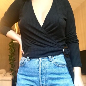Svart ribbad wrap top - Säljer denna fina toppen då den tyvärr ej passar längre. Det är en svart ribbad wrap top med ett brun-melerat häfte från NLY Trend. Köparen står för frakt