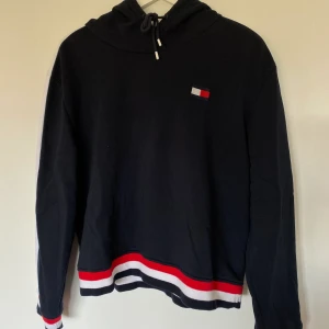 Tommy Hilfiger Hoodie - Något croppad hoodie från Tommy Hilfiger. Inköpt i TH-butik i Los Angeles för ca 700kr. Mörkblå med ränder längs armar samt på muddar. Är i storlek XL men passar M-L! Skickas spårbart för 63kr 🤩 