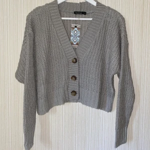 Stickad kort cardigan - Helt ny! Stickad kofta med Nedhasad Axel och knappar med färg Grå 
