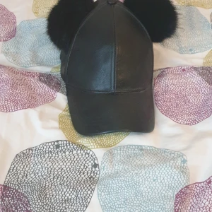 Svart keps med bollar på - En svart keps med gullar puffar på båda sidorna av kepsen