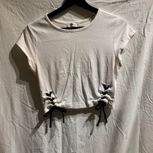 T-shirt med detalj  - En vit T-shirt med detalj i midjan vilket ger illusionen av en lite mindre midja. Väldigt fin även om den är enkel. Används inte längre och säljs därför. Plagget är i gott skick. 