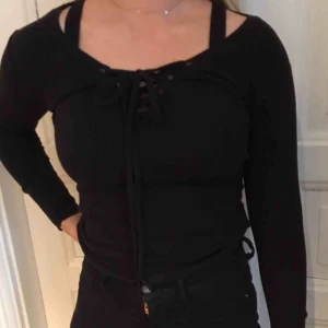  - Svart långärmad, med snören vid bysten. Passar XS till M