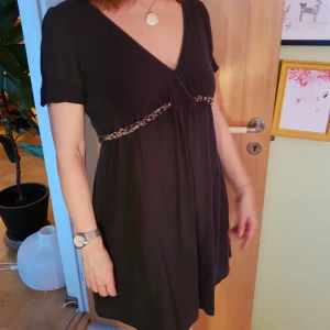  - En söt, kort klänning med djup urringning från det gamla, exklusiva märket Brittinger. Klänningen har ett slags textilskärp som knyts. Tillverkad av en blandning av viskos och bomull. I gott skick.  Går att hämtas upp i Gamla Stan eller skickas med post. 