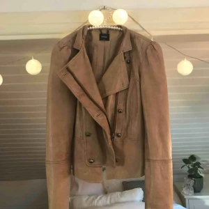  - Beige skinnjacka i läder med lite puffiga axlar och många knappar. Bra skick, Köparen står för frakt som går på 59kr annars kan jag mötas upp i Gävle.