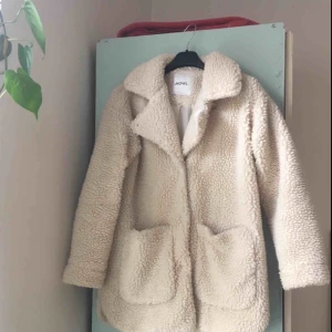  - Vit faux shearling/”Teddykappa” från Monki säljes! Nytvättad. På innersidan finns lite mörkare ”fläckar” som inte gått bort i tvätten (se bild 3) men det är alltså inget som syns utifrån :)   Storlek: XXS Använd i 1 år.
