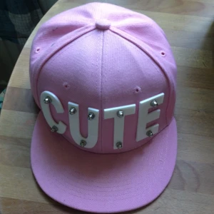  - Söt rosa keps med texten CUTE från amai.se, köpt för 229 kr. Använd en gång och har ett litet svart märke på vänstra sidan, syns på bilden. Inspänningsbar på baksidan. Köparen står för frakten.
