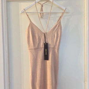  - Beige/nude klänning i fusk mocka med alla lappar kvar, fint ”knyt” rund halsen för att framhäva formen på bysten. Alla lappar kvar.