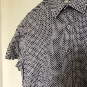 Lilamönstrad skjorta - En kortärmad skjorta i lila mönster. SAMFRAKTAR