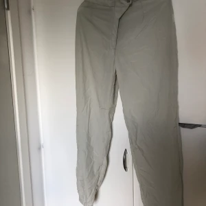 Ett par tunna ljusgråa byxor - Ett par aningen genomskinliga byxor. Dragkedja och knapp. SAMFRAKTAR