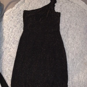 Nyårs kläning - Perfekt nyårskläning, one shoulder. Svart med guldig glitter ish. Jättesöt men aldrig använd då de inte är min stil. Storlek S