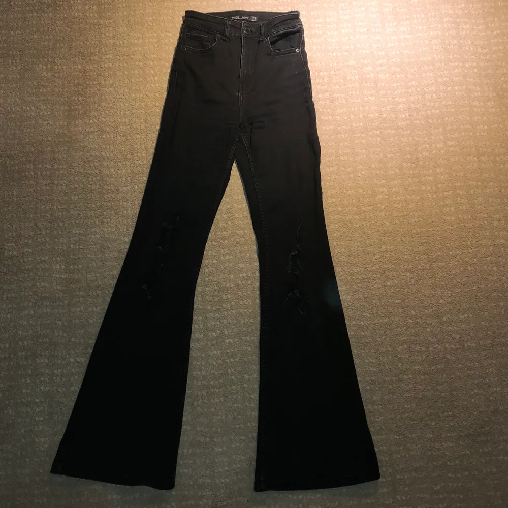 Svarta bootcut jeans från Bershka med hål på båda knäna. Jeanstyget är stretchigt och formar sig fint efter kroppen. Byxorna är använda, men fortfarande i fint skick.. Jeans & Byxor.