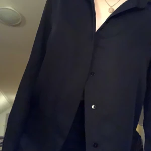 Svart skjorta - Svart skjorta i ganska tunt tyg, använd 1 gång, väldigt skönt material 