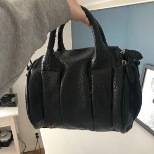  - En svart snygg väska med nitar på botten. Har dock inget väskband till men har ringar på sidorna som man kan lätt sätta på en annan på den! Har knappast använd så är som helt ny! 