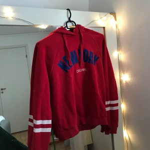 Röd hoodie - Fin röd hoodie med blå text. Köpt på Gina tricot. Bra skick men inte lika mysig inuti längre, fortfarande väldigt skönt och värmer bra. Väldigt cool egentligen, men kan inte bära upp den lika bra som jag hoppas att någon annan kan!