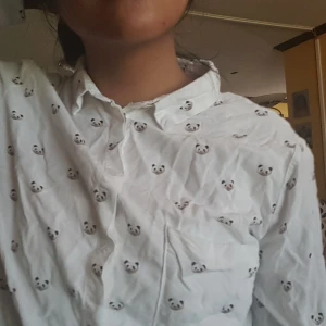 Skjorta med pandor  - Vit skjorta med panda huvuden köpt i Spanien på berska. Lite användning så säljer. I bra skick. Frakt kostar 44kr men vid snabbt köp bjuder ja på hälften av frakt kostnad. STRYKER INNAN JAG POSTAR. 