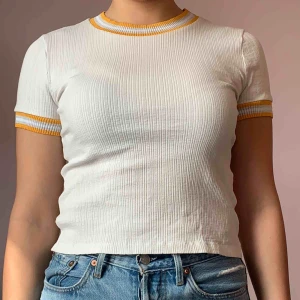  - Vit t-shirt med gul/orangea detaljer Passar till allt ifrån ett par Ripped jeans till en gullig mini-kjol🤍💛🧡