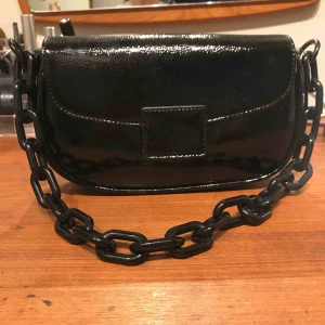  - Glansig axelbandsväska från Ginatricot med kedja. Använd men är i fint skick. 