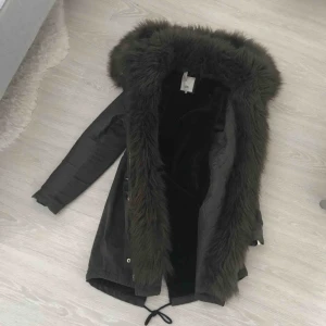 - Mörkgrön jacka med fuskpäls. 