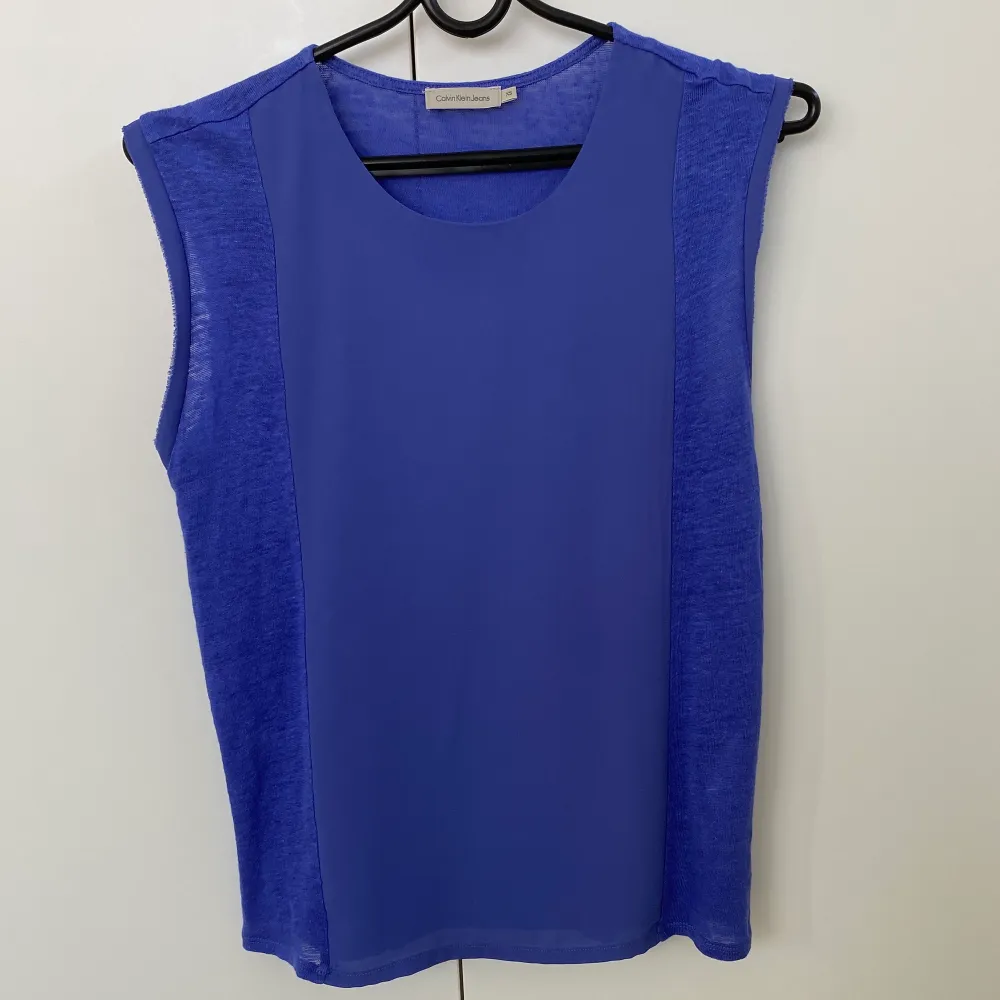 Säljer denna blå tröja utan ärmar från Calvin Klein Jeans. Väldigt fin och skön att bära under sommaren då materialet vid ärmarna och sidorna består av 100% linne medan tyget på framsidans mitt är gjord av en blandning av chiffon och polyester. . Toppar.