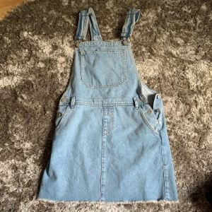Nakd jeansklänning/kjol med hängslen  - Aldrig använd, enbart testad och lappen kvar. Säljer eftersom att den inte passar mig. Priset är exklusive frakt.