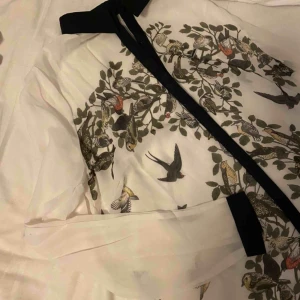  - Vit blus med fågelmotiv och svarta detaljer. Vid frakt står köparen för fraktkostnaden 