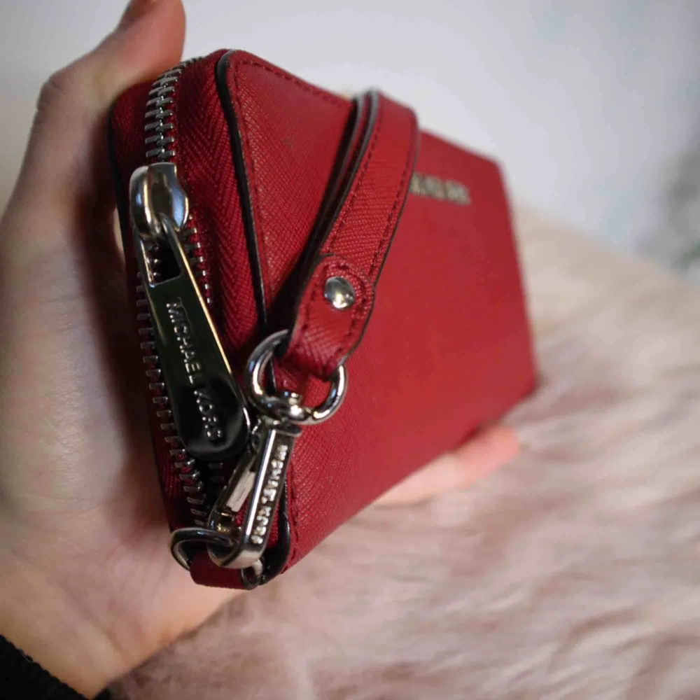 Säljer en ny plånbok från Michael Kors, modell JET SET, material crossgrain (läder) i en röd färg med silverdetaljer. Nypris 1200kr. Kan skickas med spårbar frakt mot 60kr eller mötas upp i Borås eller Kungsbacka.. Väskor.
