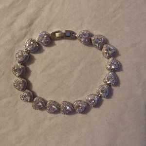  - Silvrigt armband med hjärtan. Har aldrig använts då den är lite stor på mig. Vet ej var den köptes. Kan hämtas i Lund eller Eslöv, annars tillkommer frakt.