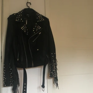  - Nitad fejk skinnjacka med fransar längst ryggen och armarna. Tyvärr har den aldrig kommit till användning så jag säljer den med taggen fortfarande på. Köpt för 1000kr. ￼