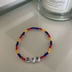 Färgglatt pärlarmband med bokstäver - Säljer ett supercoolt armband med färgglada pärlor i rött, blått och gult. Armbandet har också vita pärlor med bokstäverna 'DIF'. Perfekt för att ge lite färg till din outfit!