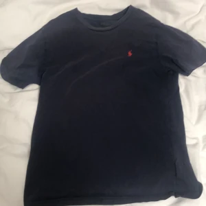 Mörkblå t-shirt från Polo Ralph Lauren - Säljer en snygg mörkblå t-shirt från Polo Ralph Lauren. Den har en liten röd broderad logga på bröstet och är i bra skick. Perfekt för en casual look!