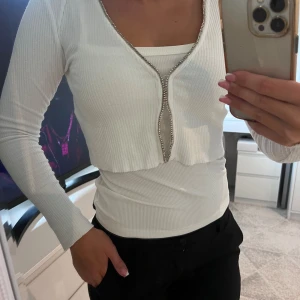Vit ribbad tröja med strassdetaljer - Snygg vit ribbad tröja med strassdetaljer från BERSHKA i storlek S. Man kan ha den både utan och med linne, uppknäppt eller ej! 