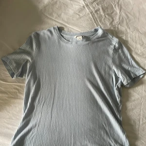 Monki T-shirt  - En ljusblå t-shirt med ribbstickning. T-shirten har en rund halsringning och korta ärmar. Storlek M  