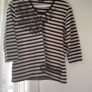 Brun/Grå Randig V-neck Tröja - Lite ”grunge” vibe med coolt mönster på. Den har lite kortare armar. Ett par av stenarna har lossnat (bild 4) men det finns inga andra defekter. Står ingen storlek men skulle säga att den är lite stor för mig som brukar ha XS/S. Köpt second hand.