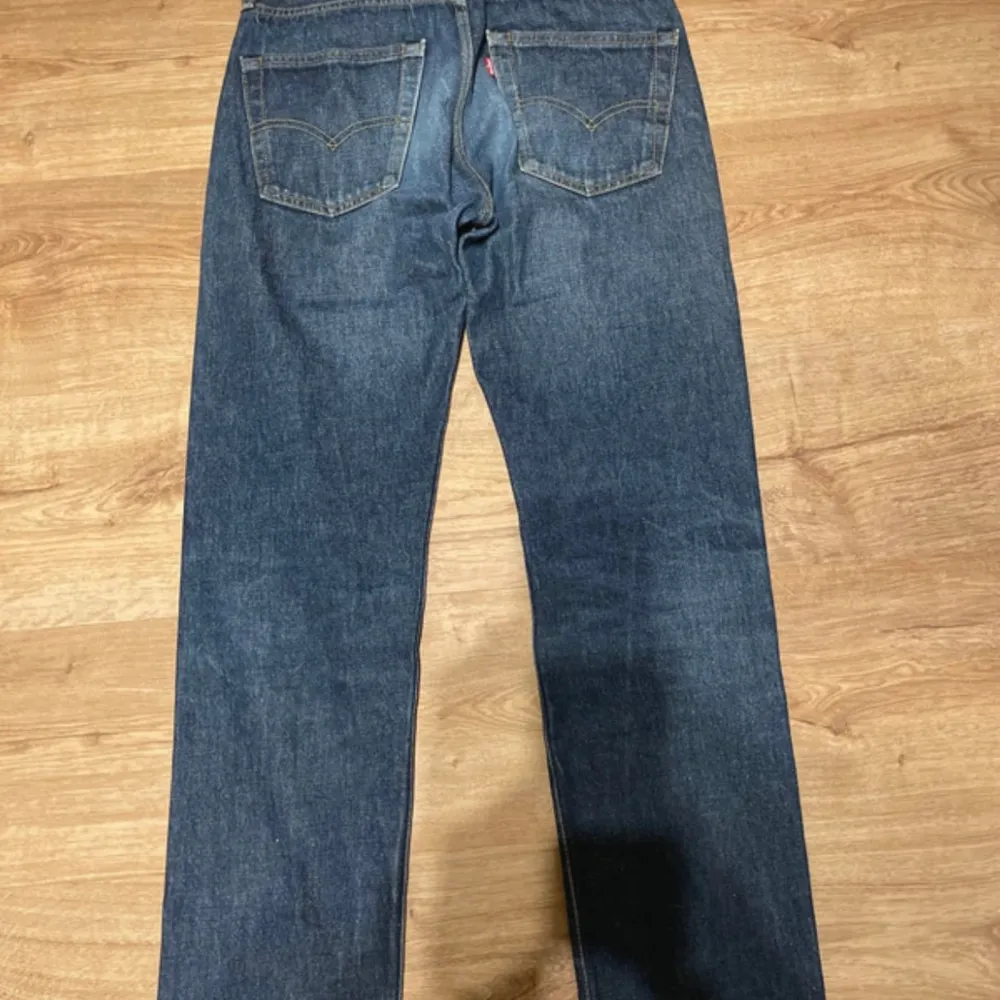 Säljer ett par klassiska Levi's 501 jeans i blå denim. De har en straight passform och är i bra skick. Perfekta för en avslappnad stil och funkar året runt. Jeansens ikoniska design med fem fickor och knappgylf gör dem tidlösa och mångsidiga. Dem har också slitningar såsom rå kant och hål i den lilla fickan. Jeans & Byxor.