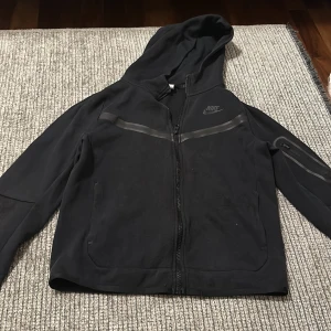 Svart hoodie från Nike - Säljer en svart hoodie från Nike i storlek L barn. Den har en dragkedja framtill och en praktisk huva. Perfekt för både träning och vardag. Den är i bra skick och redo för nya äventyr!