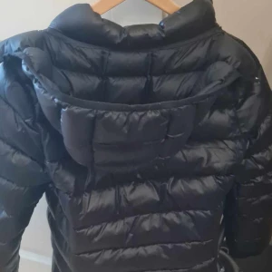 Täckjacka Polo Ralph Lauren - Täckjacka svart med luva. Varm o skön. I använt skick. En liten reva på vänsterärmen. Personen på bilden är 1,73cm.