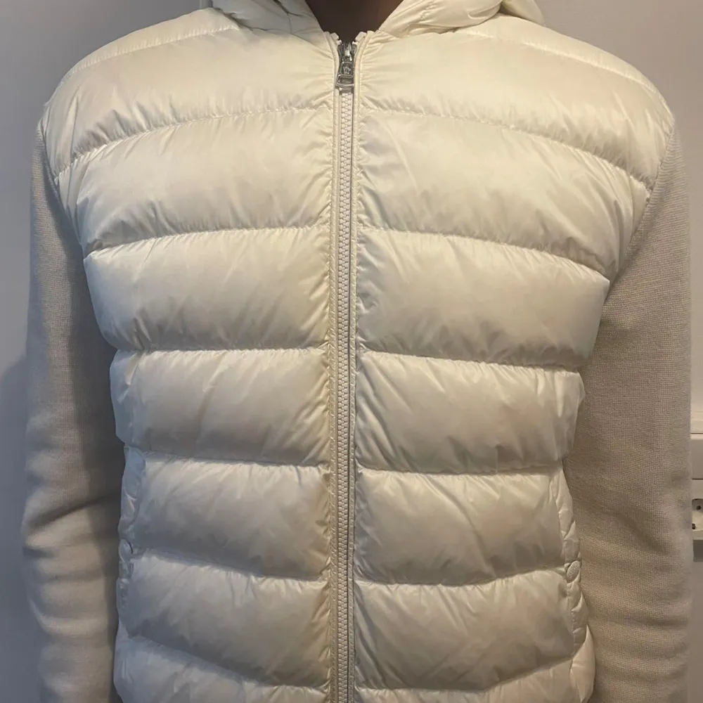 Säljer en snygg vit pufferjacka från Moncler. Jackan har en quiltad design med dragkedja framtill och en huva för extra värme. Den har långa ärmar med Monclers logga på sidan och en stilren randig detalj i rött och blått. Perfekt för kyliga dagar!. Jackor.