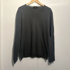 Grå tröja från Hugo Boss - Säljer en stilren grå tröja från Hugo Boss i storlek L. Den är gjord av finaste italienska garn och har en slim fit passform. Perfekt för både vardag och lite finare tillfällen. Tröjan har en klassisk v-ringning och långa ärmar. Den är i bra skick och redo för en ny ägare!