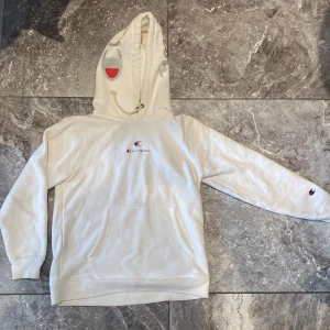 Vit hoodie från Champion - Säljer en supermysig vit hoodie från Champion. Den har en klassisk känguruficka och justerbar huva med dragsko. Champion-loggan syns både på bröstet och ärmen. Perfekt för en chill dag eller när du vill ha något bekvämt och stilrent. Passar till allt!
