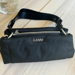 Handväska Ganni - Ganni Pillow Pillow Baguette Black  Nyskick och knappt använd  Nypris: 2295kr  Pris nu: 1000kr  Kvitto finns   Material : 70% Recycled Polyamide 30% Recycled Leather Storlek:  H: 11 cm, B: 25 cm, D: 10cm Längd på handtag: 24 cm